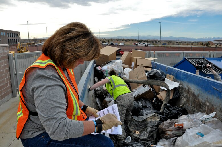 Gretchen Myers, 460th Space Wing Plans and Programs office plans analyst, left, reviews found documents while 1st Lt. Liz Dunsworth, 460th SW XP chief Crisis Action Team director, continues to search a dumpster Nov. 8, 2013, on Buckley Air Force Base, Colo. This search was part of an ongoing project ensuring the base is following all operations security measures and preventing unauthorized access to secret and personal information. (U.S. Air Force photo by Staff Sgt. Nicholas Rau/Released)