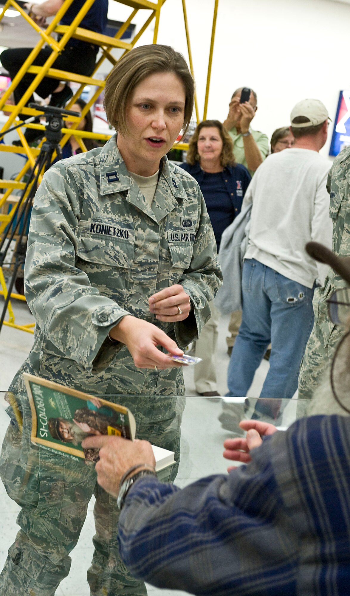 Capt. Tracie Konietzko, 57th Information Aggressor Squadron Threat Flight commander, gives Si Robertson, Duck Dynasty star, her squadron coin during his book signing at the Exchange Nov. 12, 2013, at Nellis Air Force Base, Nev. Many fans presented Si with gifts such as squadron coins, cards and photographs. (U.S. Air Force photo by Senior Airman Matthew Lancaster)
