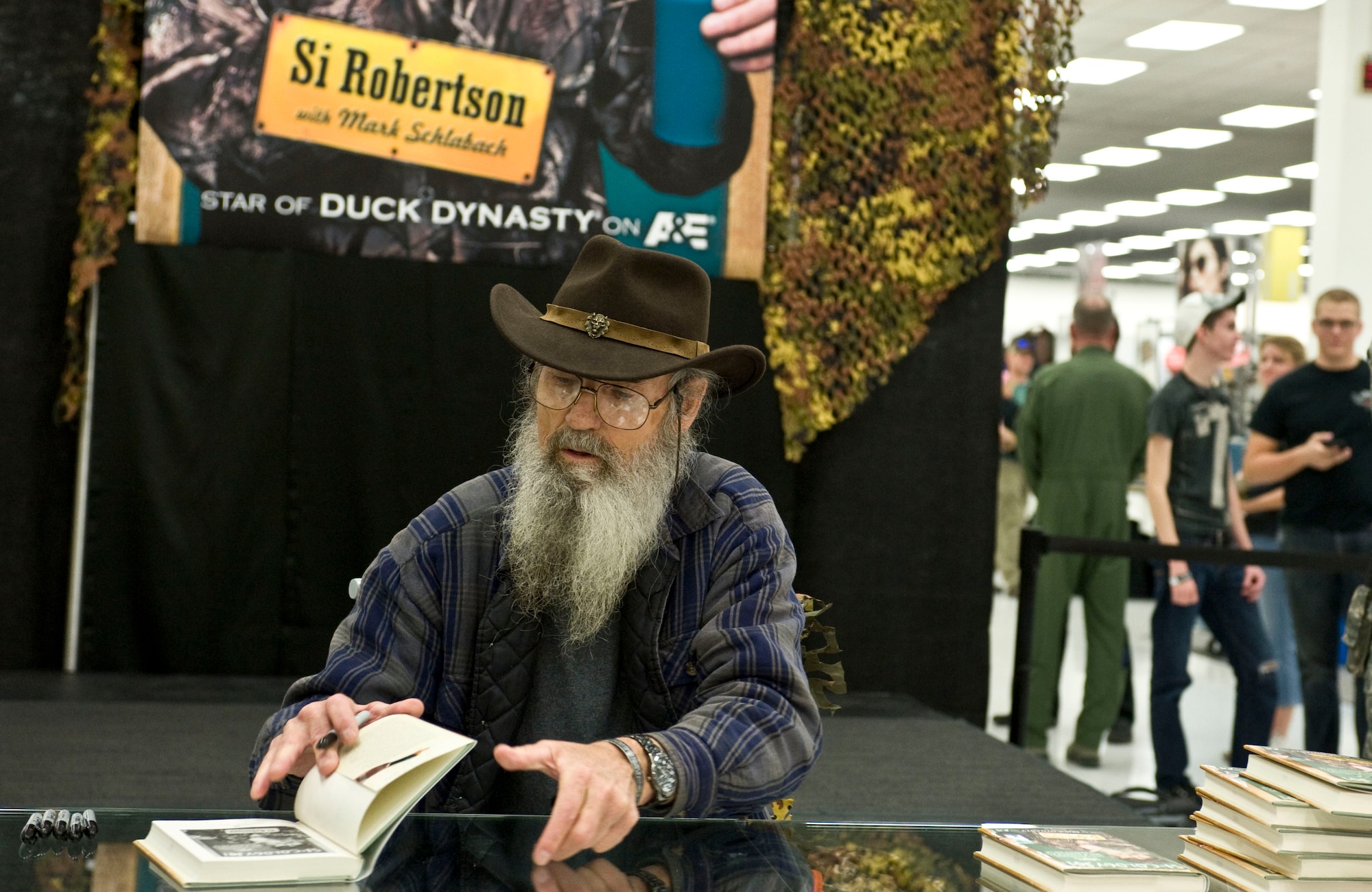 Si Robertson, Duck Dynasty star, autographs copies of his book “Si-cology 1: Tales and Wisdom from Duck Dynasty's Favorite Uncle” during his book signing at the Exchange Nov. 12, 2013, at Nellis Air Force Base, Nev.  Robertson, often referred to as Uncle Si, is a television personality, preacher, hunter, outdoorsman and employee at duck call maker Duck Commander. (U.S. Air Force photo by Senior Airman Matthew Lancaster)