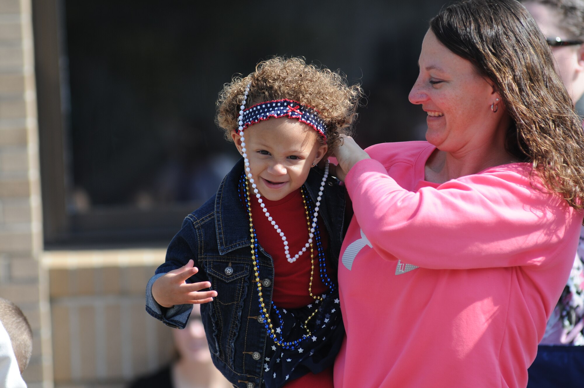 Master Sgt. Laurie Holmes, 334th Training Squadron, puts a set of beads around her daughter’s neck during the 13th Annual Gulf Coast Veteran’s Day Parade in front of City Hall Nov. 9, 2013, Biloxi, Miss.  Keesler’s Wing leadership, Honor Guard, and Airmen, who carried the 50 State Flags, participated in the event. (U.S. Air Force photo by Kemberly Groue)