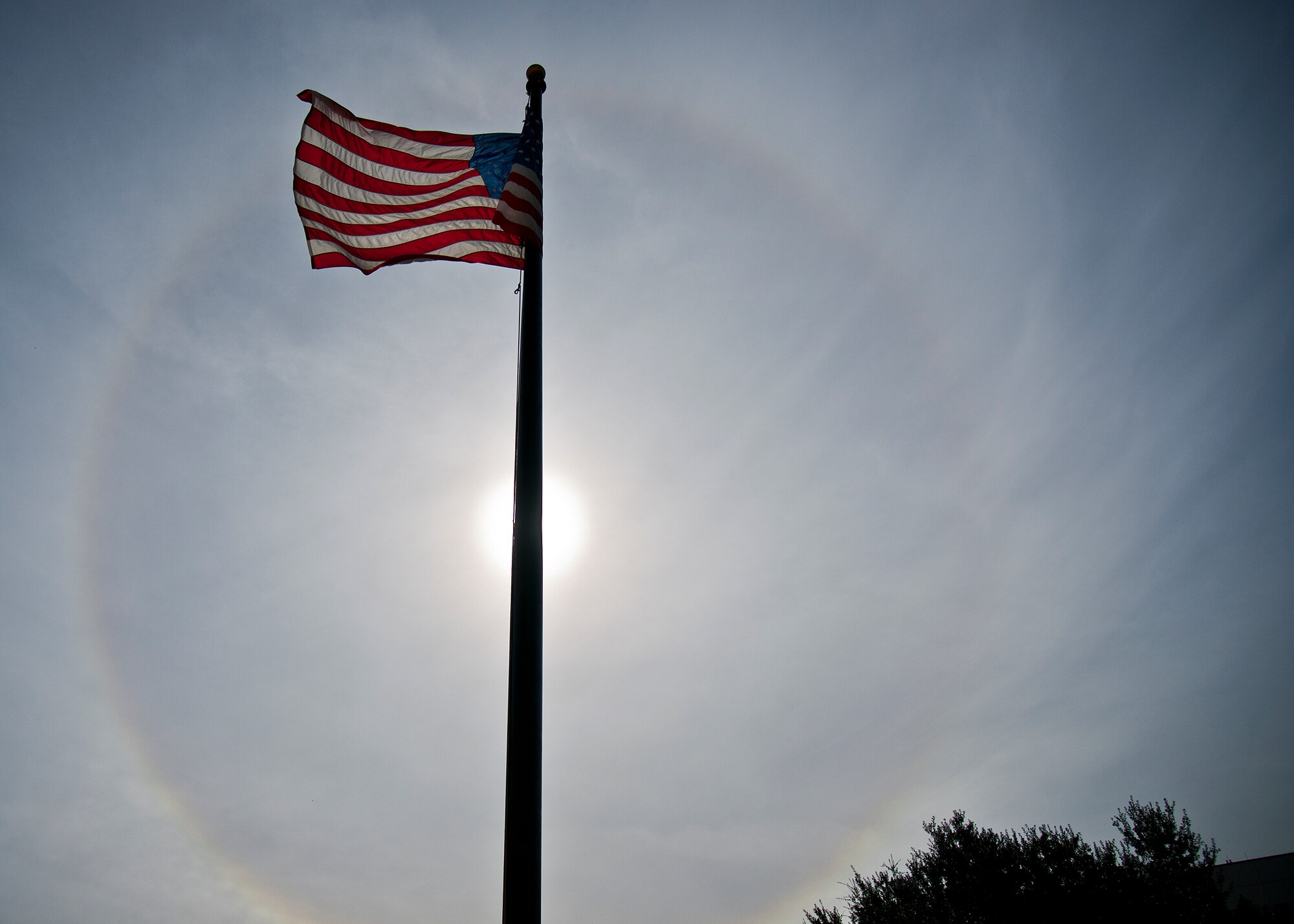The American Flag flies below a giant solar halo in the sky over the Building 351 in the early afternoon Nov. 12 at Eglin Air Force Base, Fla. The optical phenomenon is caused by ice crystals in the atmosphere.  (U.S. Air Force photo/Samuel King Jr.)