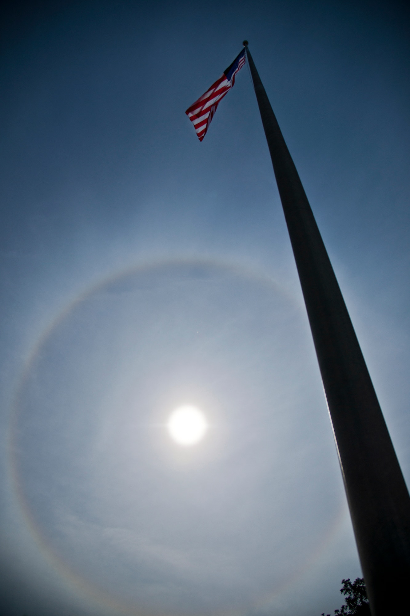 The American Flag flies below a giant solar halo in the sky over Building 1 in the early afternoon Nov. 12 at Eglin Air Force Base, Fla. The optical phenomenon is caused by ice crystals in the atmosphere.  (U.S. Air Force photo/Samuel King Jr.)