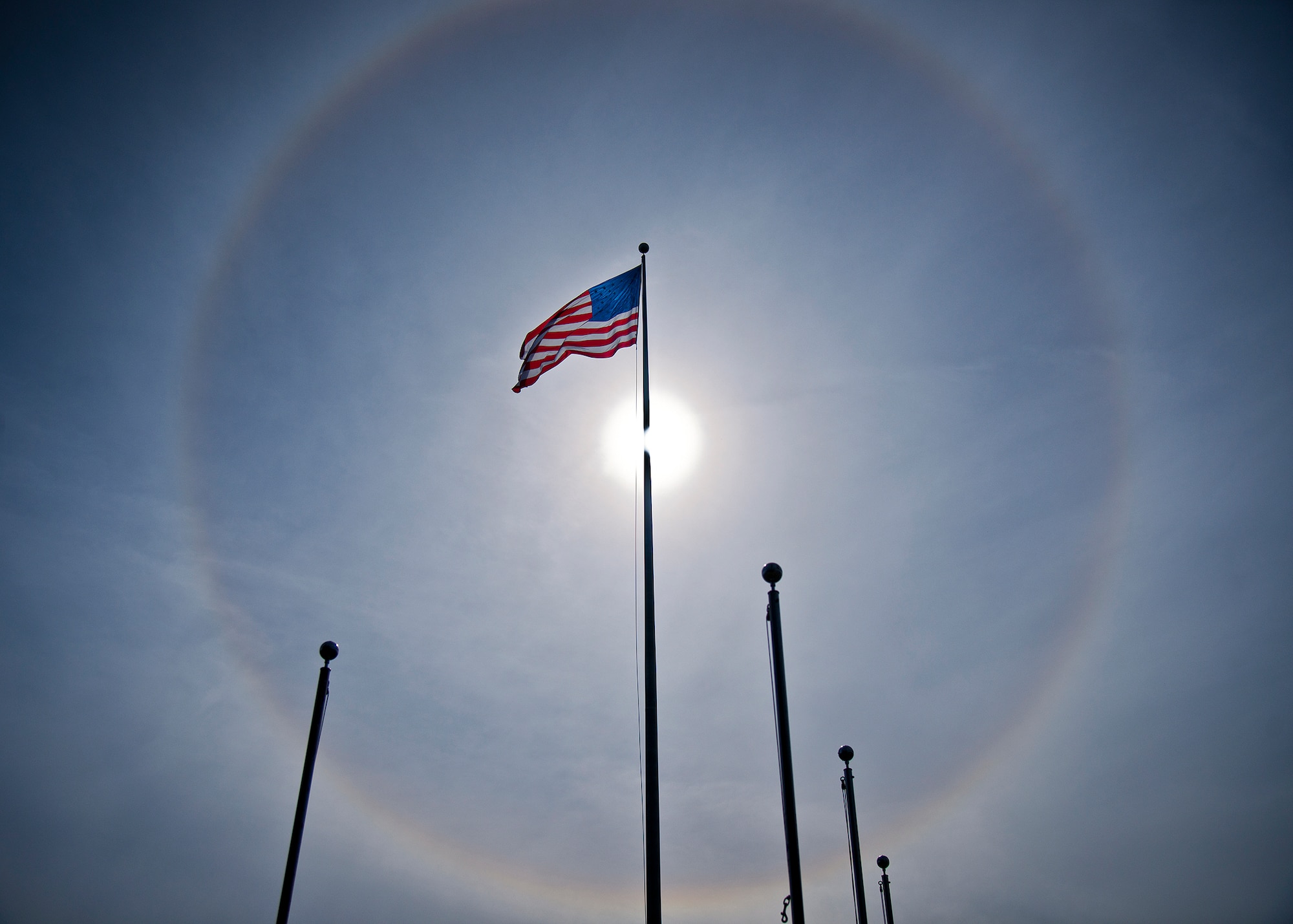 The American Flag flies below a giant solar halo in the sky over Building 1 in the early afternoon Nov. 12 at Eglin Air Force Base, Fla. The optical phenomenon is caused by ice crystals in the atmosphere.  (U.S. Air Force photo/Samuel King Jr.)