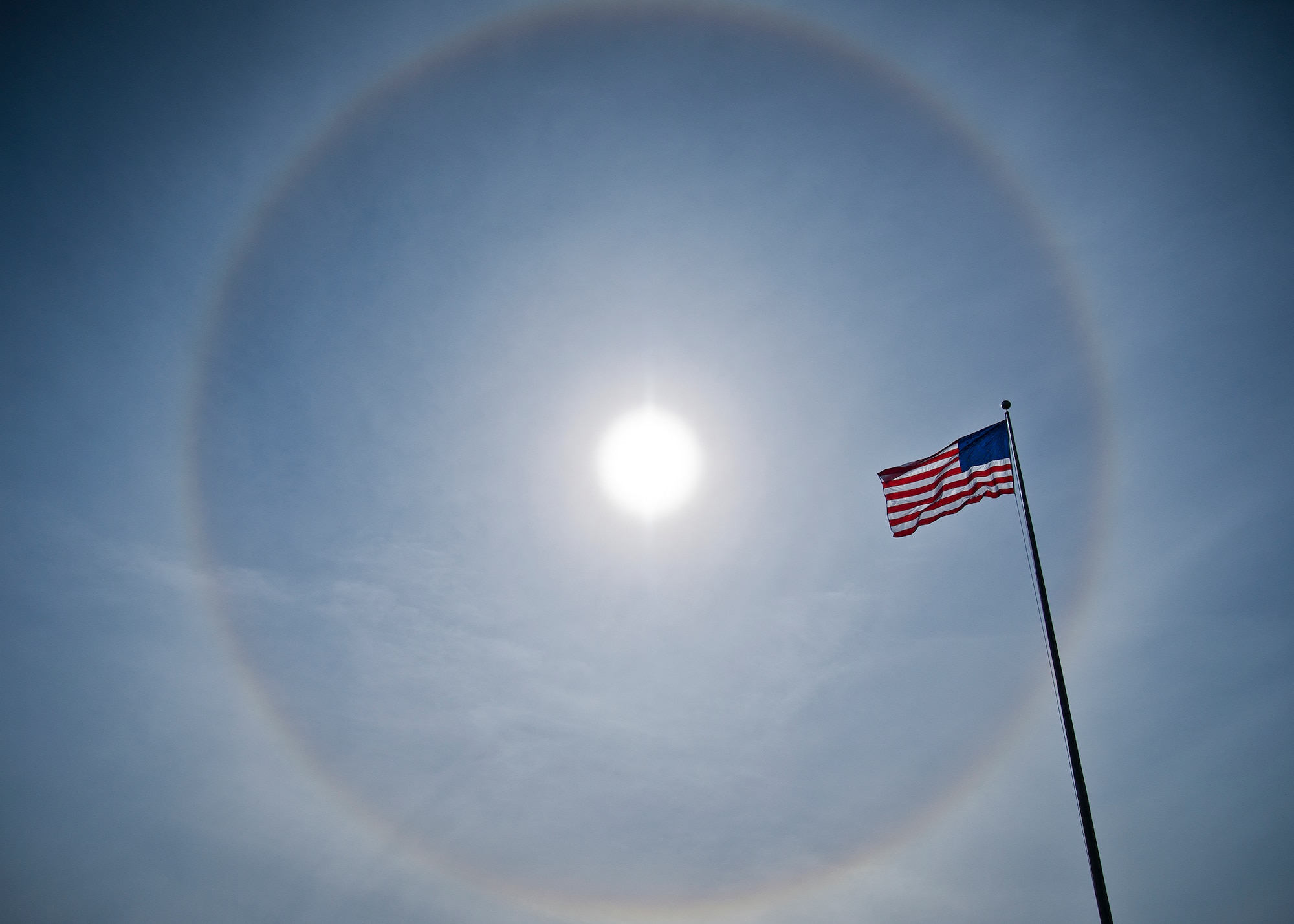 The American Flag flies below a giant solar halo in the sky over Building 1 in the early afternoon Nov. 12 at Eglin Air Force Base, Fla. The optical phenomenon is caused by ice crystals in the atmosphere.  (U.S. Air Force photo/Samuel King Jr.)