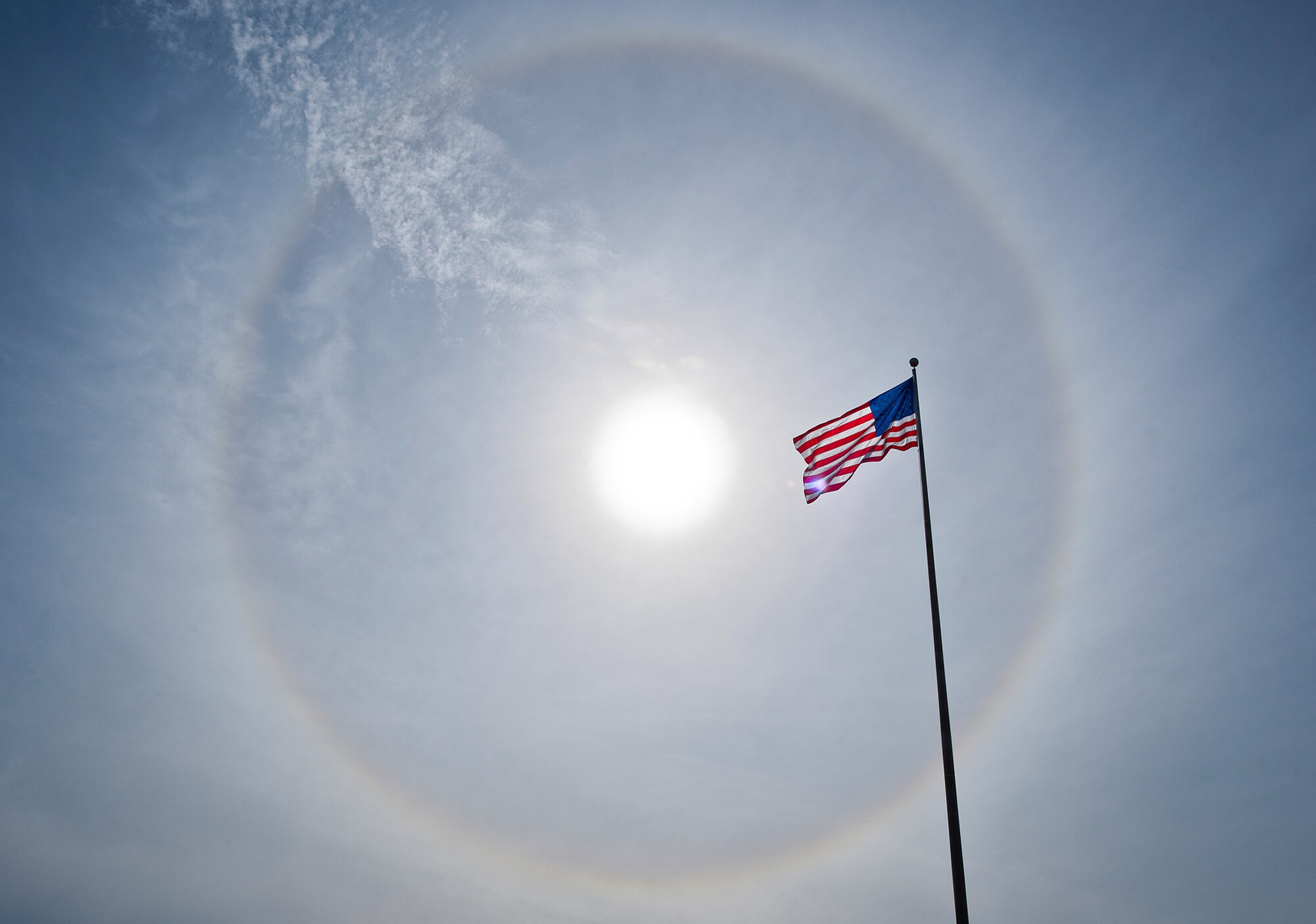 The American Flag flies below a giant solar halo in the sky over Building 1 in the early afternoon Nov. 12 at Eglin Air Force Base, Fla. The optical phenomenon is caused by ice crystals in the atmosphere.  (U.S. Air Force photo/Samuel King Jr.)