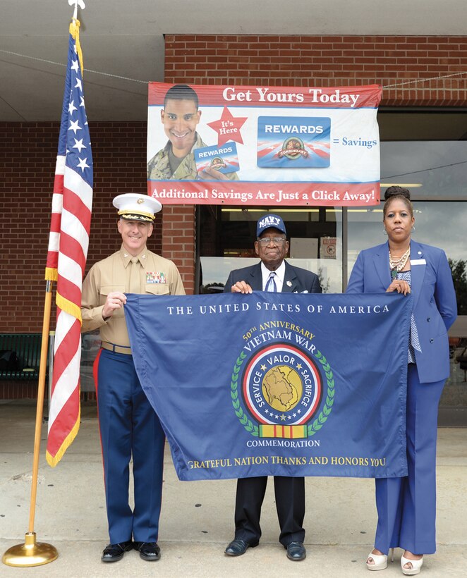 Col. Don Davis, commanding officer, Marine Corps Logistics Base Albany, holds a flag, which commemorates the 50th anniversary of the Vietnam War in front of MCLB Albany’s Commissary, Nov. 5. The flag was also held by J. D. Armstrong, U.S. Navy retired and Vietnam veteran, and Cynthia S. Blair, store director, Commissary, MCLB Albany.