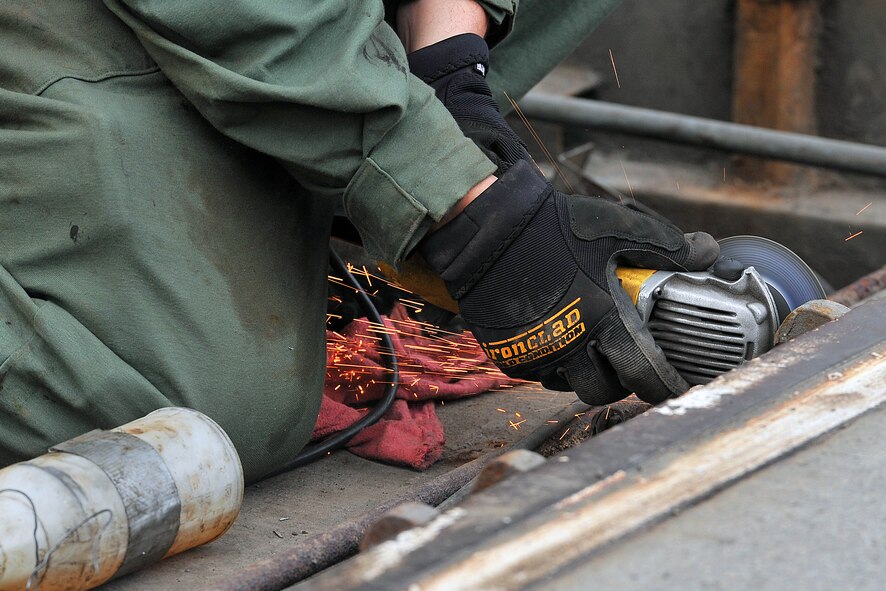 Senior Airman Christian Acosta, 92nd Civil Engineer Squadron structure shop, grinds medal by the front gate Nov. 13, 2013, at Fairchild Air Force Base, Wash. The pop-up barriers require maintenance at least once a year. (U.S. Air Force photo by Staff Sgt. Veronica Montes)  
