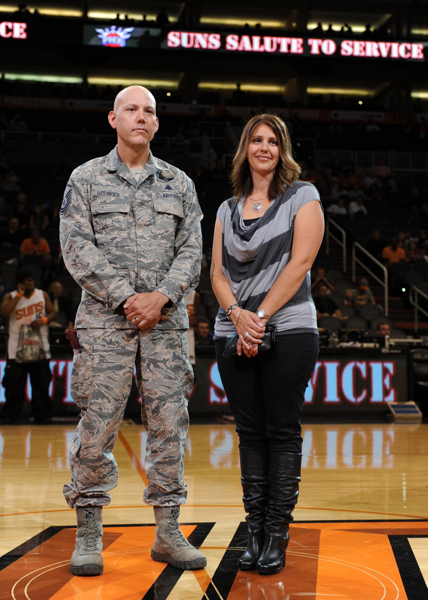 Master Sgt. David Biddinger, 48th Rescue Squadron pararescueman, assigned to Davis-Monthan Air Force Base, and his wife, Teresa Biddinger, stand center-court inside US Airways Center, Phoenix, Ariz during a Phoenix Suns game Nov. 10, 2013. MSgt. Biddinger was honored during half-time for the critical medical assistance that he and seven other Airmen provided during the deadly 19-vehicle accident on I-10 near Picacho Peak, Oct. 29, 2013. (U.S. Air Force Photo by Airman 1st Class Chris Massey/Released)(cropped)