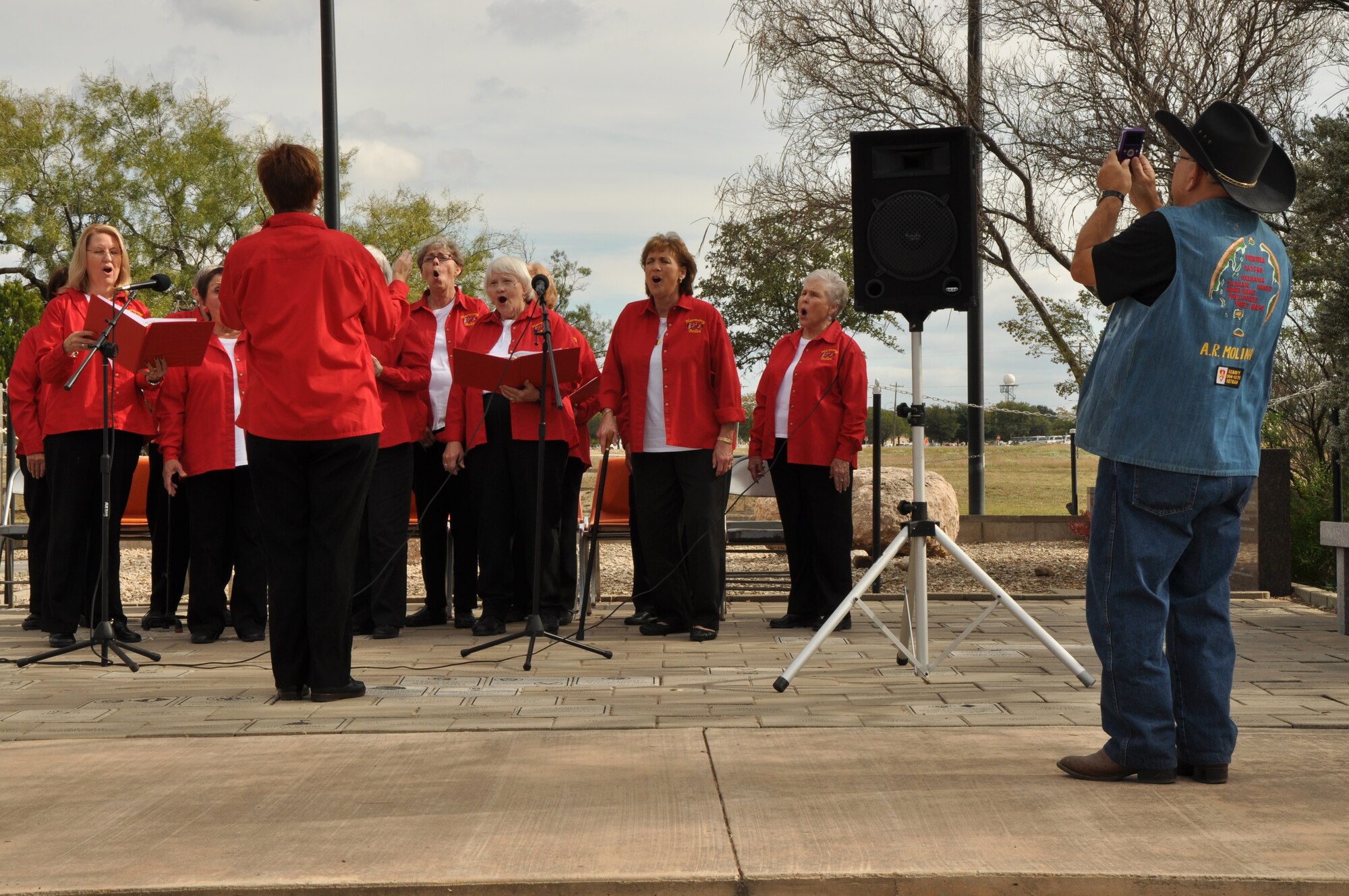 SAN ANGELO, Texas – Retired Navy Petty Officer 2nd Class Amado Melina, Vietnam War veteran, records the Harmony Belles, a non-profit San Angelo choir, as they sing God Bless America during the Veterans Day observance at the Mathis Field Vietnam Memorial Nov. 11. The Harmony Belles also sang several other historical patriotic songs. (U.S. Air Force photo/ Airman 1st Class Joshua Edwards)
