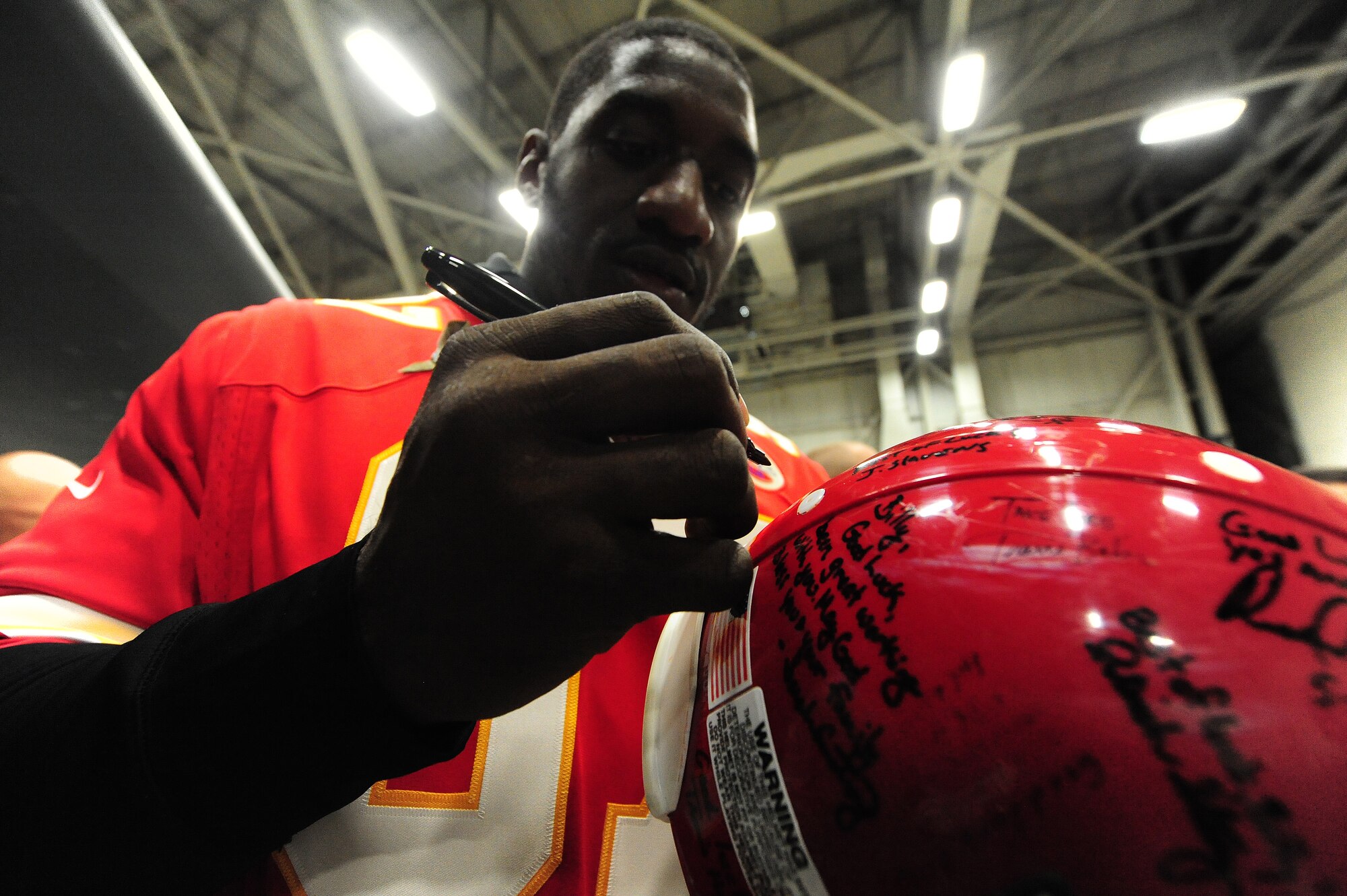Allen Bailey, a defensive tackle for the Kansas City Chiefs, signs a helmet for a fan during a B-2 tour at Whiteman Air Force Base, Mo., Nov. 12, 2013. In addition to the B-2 tour Bailey, four other chiefs players and two Chiefs cheerleaders visited Whiteman Elementary School to talk to the children about the importance of living an active lifestyle and to demonstrate various workouts and football drills. (U.S. Air Force photo by Staff Sgt. Nick Wilson/Released)