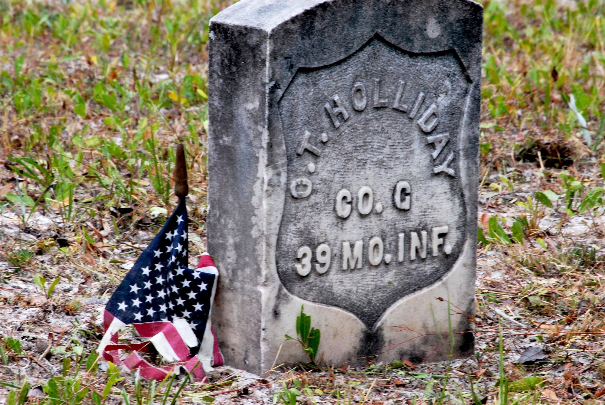 A weathered flag drapes the stars and stripes over an aged headstone at Marywood Cemetery. Marywood Cemetery is one of eleven grave sites at Tyndall. (U.S. Air Force photo by 2nd Lieutenant Christopher Bowyer-Meeder)