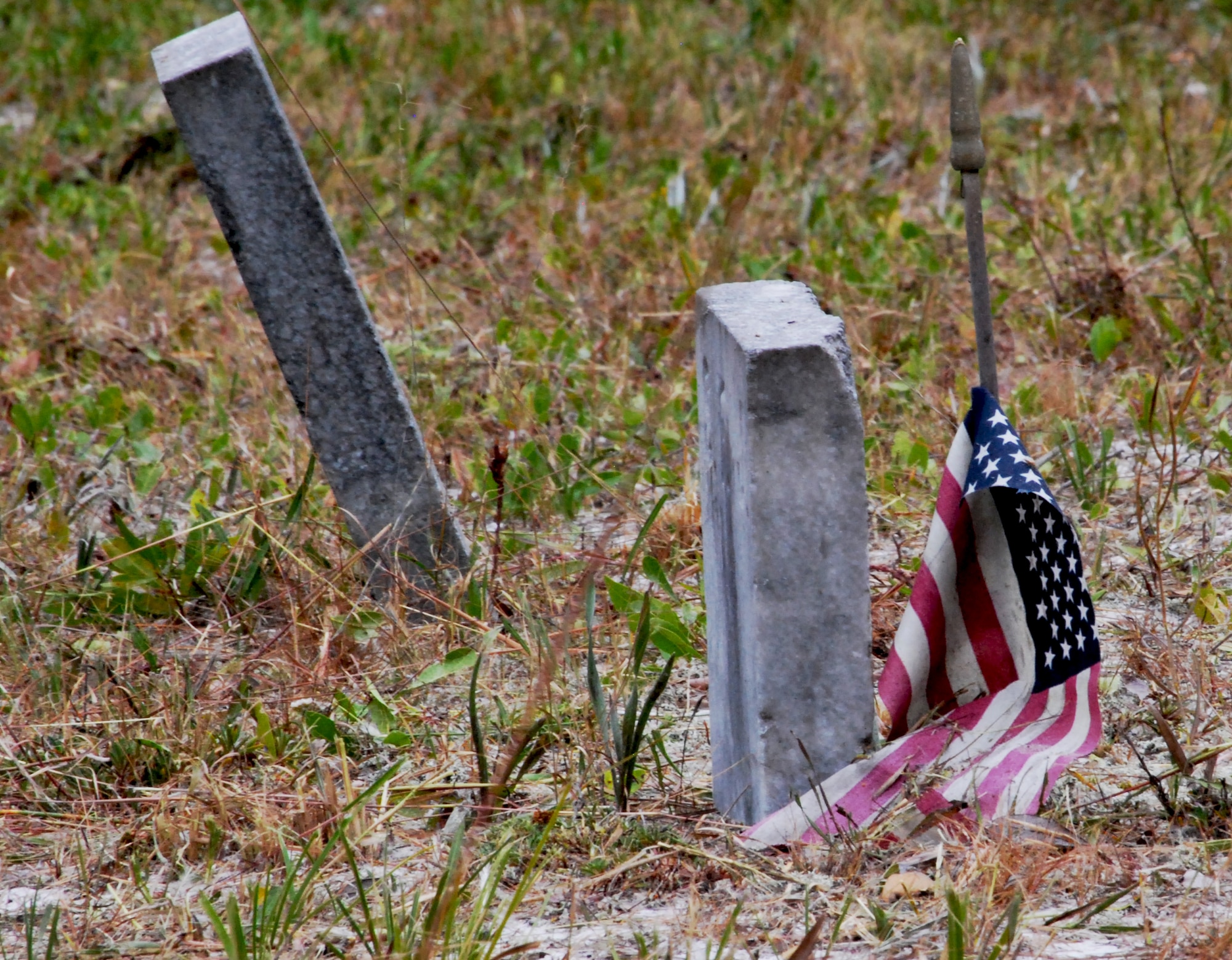 A weathered flag drapes the stars and stripes over an aged headstone at Marywood Cemetery. Marywood Cemetery is one of eleven grave sites at Tyndall. (U.S. Air Force photo by 2nd Lieutenant Christopher Bowyer-Meeder)