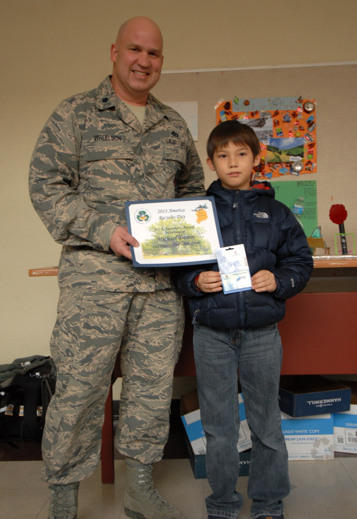 Lt. Col. Jack Wheeldon, 51st Civil Engineer Squadron commander, presents Michael Destin with the second place award in his age group for the recycled art contest held at Osan Air Base, Republic of Korea, Nov. 14, 2013. The contest was used to raise awareness of America Recycles Day, held every year on Nov. 15. (U.S. Air Force photo / 1st Lt. Kay M. Nissen)