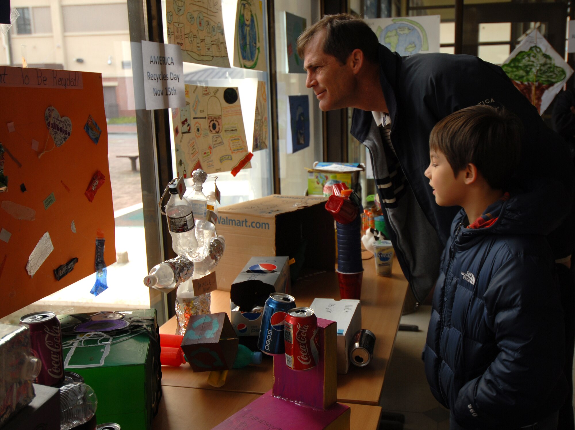 Michael Destin and son, Michael, check out the recycled art display at Osan Air Base, Republic of Korea, Nov. 14, 2013. The art projects were used to commemorate America Recycles Day, which is a day set aside to raise recycling awareness and identify the benefits of making resources available to future generations. (U.S. Air Force photo/1st Lt. Kay M. Nissen)