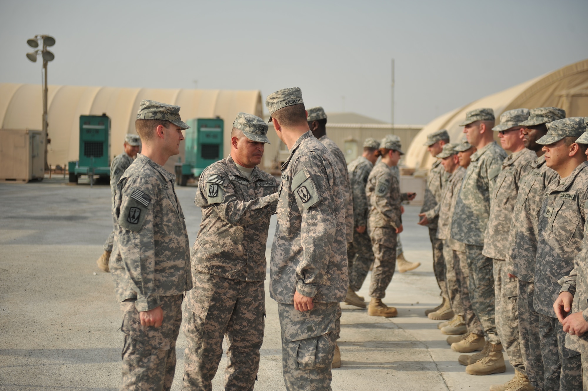 Maj. Ryan Parker looks on as Master Sgt. Jose Cruz affixes the 31st Air Defense Artillery Brigade patch to Spc. Dacoda Worth’s right sleeve at the 379th Air Expeditionary Wing in Southwest Asia Nov. 2, 2013. The date marked an important time in the 31st ADA’s deployment, as they were authorized to wear their unit patch on their right sleeve identifying them as “combat veterans.” Parker, Cruz and Worth are deployed here from Ft. Sill, Okla., and are natives of Fairless Hills, Pa.; Coamo, Puerto Rico; and Indianapolis, In., respectively. (U.S. Air Force photo/Master Sgt. David Miller)