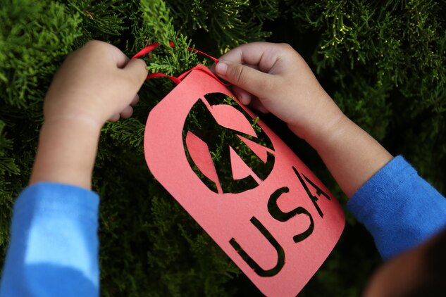 A student from Matthew C. Perry Elementary School aboard Marine Corps Air Station Iwakuni, Japan, hangs their handmade ornament on the tree located outside the school’s entrance for the Veterans Day ceremony Nov. 6, 2013. Children ages 3-12 participated in the event by making an ornament for a veteran they know.