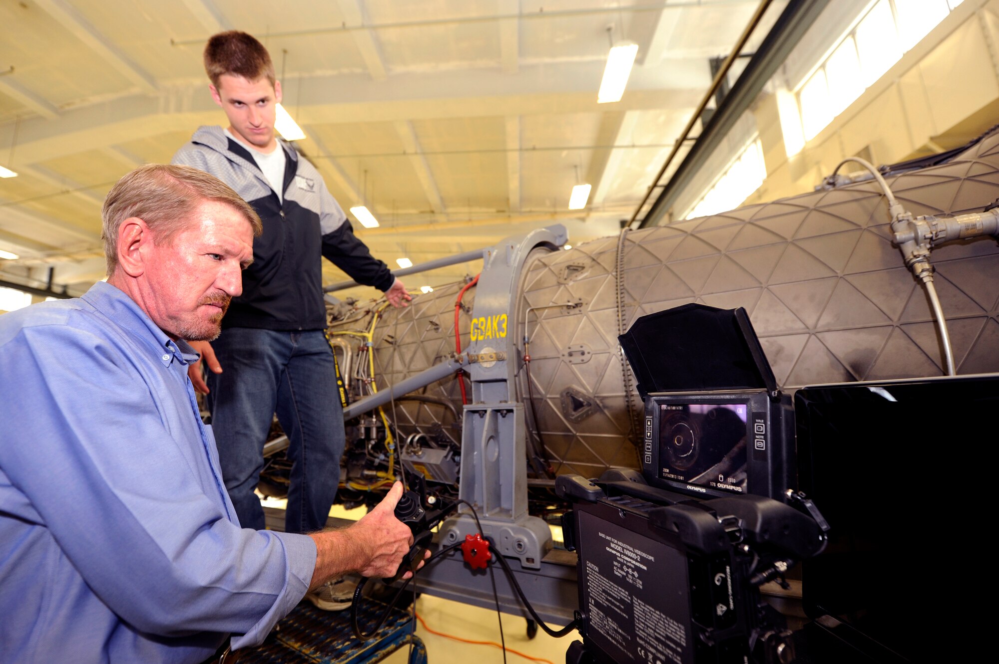 Tim Fullerton, Pratt and Whitney field representative and liaison for 18th Component Maintenance Squadron propulsion maintenance, teaches Caleb Silvers how to use a boroscope to look for problems inside an aircraft engine on Kadena Air Base, Japan, Nov. 14, 2013. During the tour of the 18th CMS propulsion shop, Kadena HS Air Force Junior Reserve Officer Training Course students, who aspire to be future engineers, were taught about different components and functions of F-15 Eagle and A-10 Thunderbolt II aircraft engines. Silvers is a JROTC student from Kadena High School. (U.S. Air Force photo by Senior Airman Maeson L. Elleman)