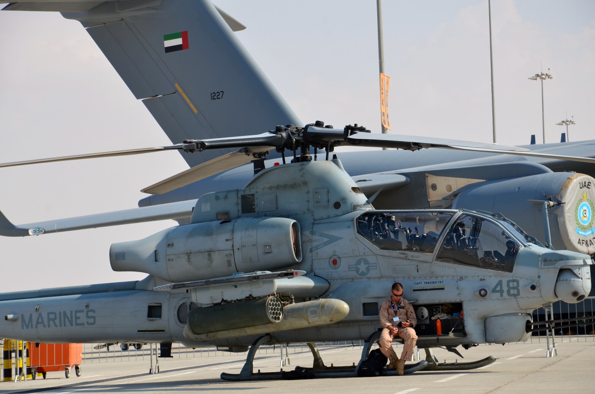 U.S. Marine Corps Capt. James Kerrigan takes a break from the desert sun at the biennial Dubai Airshow at Dubai World Central airport in Jebel Ali, United Arab Emirates, Nov. 16, 2013. A U.A.E. C-17 taxis into position behind the Cobra. Kerrigan is an AH-1Z Cobra Attack Helicopter pilot assigned to VMM 1-66 of the 13th Marine Expeditionary Unit deployed from Camp Pendleton, Calif., and calls San Diego home. Department of Defense officials stated the Dubai Airshow highlights DOD aviation technology as well as the men and women who serve. The U.S. participates in DAS to demonstrate a commitment to regional security, to demonstrate the flexibility of air power, and to strengthen military to military relationships with regional partners. All DOD forces participating in the airshow were already deployed in the region. (U.S. Air Force photo/Maj. David Faggard)