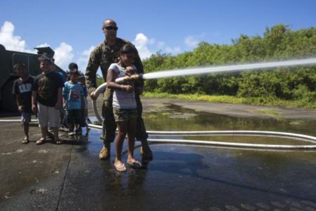 Lance Cpl. Joseph Alvarez, from Redlands, CA., helps a local child use the fire-hose Nov. 11, after a Veterans Day and Marine Corps Birthday ceremony Nov. 11 at Tinian’s Historic North Field during exercise Forager Fury II. The ceremony introduced Marine Corps customs to the people of Tinian and allowed the Marines and Tinian citizens to enjoy themselves during FF II. Alvarez is a crew chief with Marine Wing Support Squadron 171, Marine Aircraft Group 12, 1st Marine Aircraft Wing, III Marine Expeditionary Force.