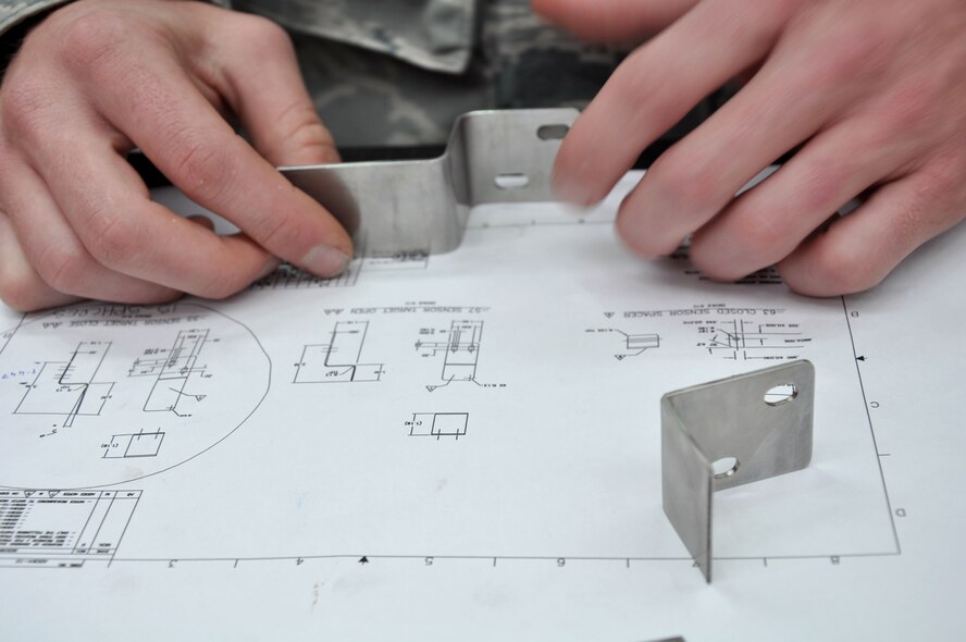 U.S. Air Force Staff Sgt. Tyrell Pennington examines a newly-crafted auxiliary power unit inlet door target sensor that Royal New Zealand Air Force Karl Waiaraki fabricated at the RNZAF Base Ohakea’s Maintenance Support Squadron Structural Repair Bay Nov. 13 in Ohakea, New Zealand. Members of the 517th Expeditionary Airlift Squadron enlisted the aid of RNZAF structural technicians to craft the piece which was causing a U.S. Air Force C-17 Globemaster III to be grounded. The Airmen and C-17 are deployed in support of Exercise Kiwi Flag. Kiwi Flag is a multilateral RZNAF-sponsored tactical airlift exercise conducted annually in New Zealand. Service members from the USAF, RNZAF, Royal Australian Air Force, Republic of Singapore Armed Forces and French Armed Forces of New Caledonia are participating. Air operations will be conducted out of RNZAF Base Ohakea, New Zealand. Kiwi Flag personnel will provide air support to Exercise Southern Katipo, New Zealand Defence Force’s largest-ever multilateral joint force amphibious exercise with eight other nations participating: United States Army and Marines, Australia, Canada, France, Malaysia, Singapore, Papua New Guinea and Tonga. Pennington, a flying crew chief, is deployed from Joint Base Elmendorf-Richardson, Alaska. He calls Los Angeles home. (U.S. Air Force photo by Senior Master Sgt. Denise Johnson)