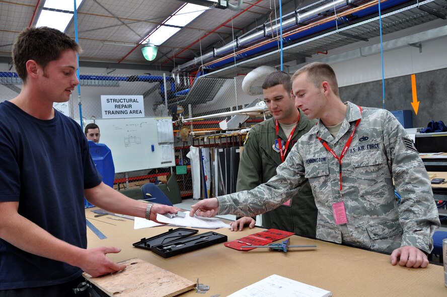 U.S. Air Force Tech. Sgt. Chris Chamberlin, flying crew chief, looks on as Royal New Zealand Air Force Leading Aircraftsman, Karl Waiariki, hands a newly-crafted auxiliary power unit inlet door target sensor to U.S. Air Force Staff Sgt. Tyrell Pennington, flying crew chief, at the RNZAF Base Ohakea’s Maintenance Support Squadron Structural Repair Bay Nov. 13 in Ohakea, New Zealand. The RNZAF structural aircraft technicians crafted the part for a U.S. Air Force C-17 Globemaster III deployed in support of Exercise Kiwi Flag. Kiwi Flag is a multilateral RZNAF-sponsored tactical airlift exercise conducted annually in New Zealand. Service members from the USAF, RNZAF, Royal Australian Air Force, Republic of Singapore Armed Forces and French Armed Forces of New Caledonia are participating. (U.S. Air Force photo by Senior Master Sgt. Denise Johnson)