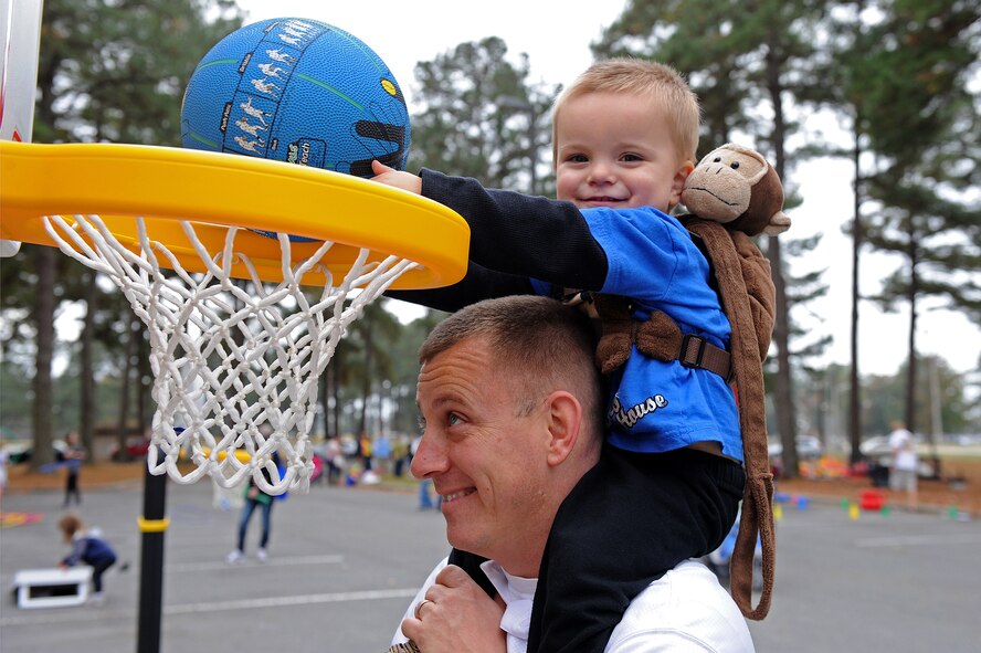 U.S. Air Force Master Sgt. Travis Clawson, 4th Civil Engineer Squadron systems fire chief, hoists his son to make a basket during the Month of the Military Family block party at Seymour Johnson Air Force Base, N.C., Nov. 16, 2013. The event featured stations for children to get involved, including basketball, corn hole and an oversized checker board. (U.S. Air Force photo by Airman 1st Class Aaron J. Jenne)