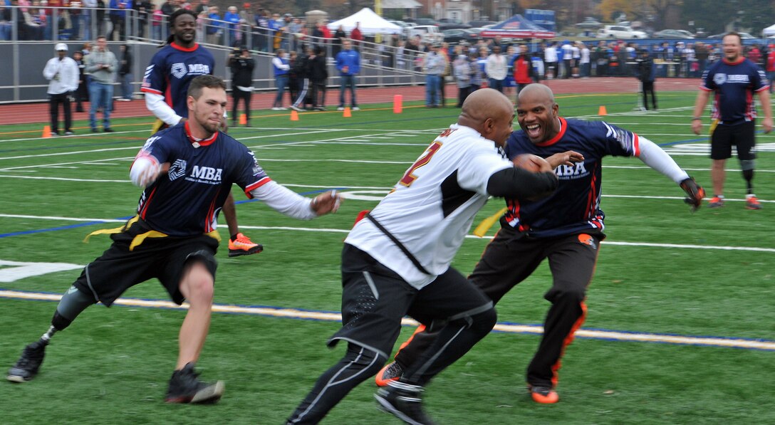 Former Washington Redskins star Brian Mitchell tries to move around former Cleveland Browns player Eric Metcalf as an amputee player rushes in to yank the flag off Mitchell during a Warrior Care Month flag football game at Bishop O'Connell High School in Arlington, Va., Nov. 16, 2013. Sponsored by the nonprofit Military Benefit Association, $60,000 was raised for the amputees. U.S. Army photo by J.D. Leipold