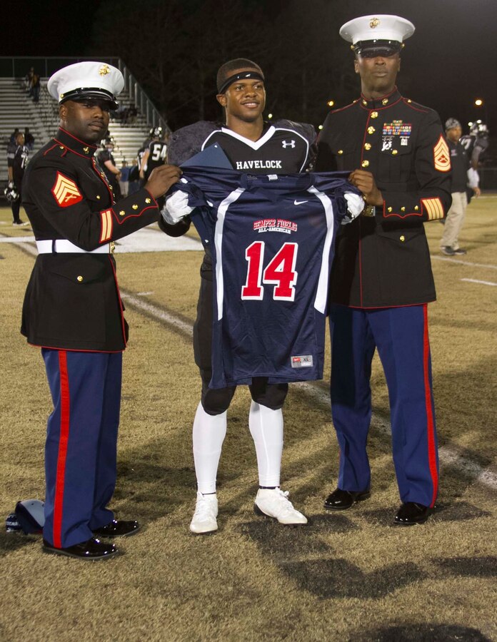 U.S. Marine Corps Sgt. Jarvis Walker, left, a recruiter with Marine Corps Recruiting Sub- Station Jacksonville, and U.S. Marine Corps Gunnery Sgt. Dwayne Williams, the staff noncommissioned officer in charge of Recruiting Sub Station Jacksonville, present Derrell Scott, a running back for the Havelock High School football team, with a jersey during his Semper Fidelis All-American Bowl jersey presentation at Havelock High School in Havelock, N.C., Nov. 15, 2013. Scott was selected to play in the bowl for his skill as a defensive end, his academics and his leadership ability.  The Semper Fidelis All-American Bowl allows the Marine Corps to purposefully engage well-rounded student athletes to share leadership lessons that will enable future success. The Bowl will be played on Jan. 5, 2014, in Carson City, Calif., and will be broadcast on Fox Sports 1. (U.S. Marine Corps photo by Sgt. Dwight A. Henderson/Released) 