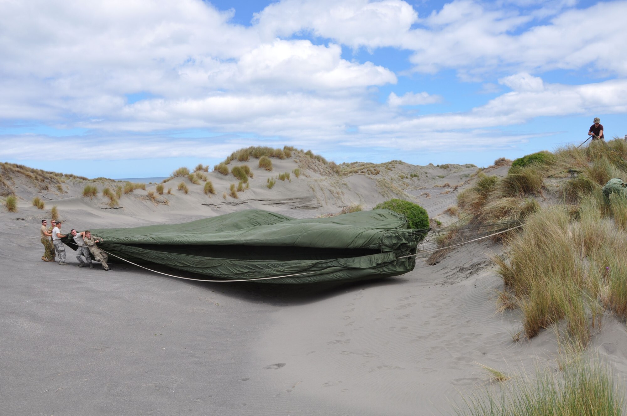 OHAKEA, New Zealand -- Multinational service members begin recovering the parachute from tactically-air-dropped cargo which landed just east of the drop zone during Exercise Kiwi Flag Nov. 14 at the New Zealand Defence Force Raumi Drop Zone near Ohakea, New Zealand. Recovery personnel from the United States Air Force, Royal Australian Air Force, Republic of Singapore Armed Forces, Royal New Zealand Air Force and New Zealand Army make their way to the main parachute amid the rolling sand dunes nestled between a pine forest and the coastline. Kiwi Flag is a multilateral Royal New Zealand Air Force-sponsored tactical airlift exercise comprising air assets from the USAF, RNZAF, RAAF, RSAF and French Armed Forces of New Caledonia. (U.S. Air Force photo by Senior Master Sgt. Denise Johnson/Released)
