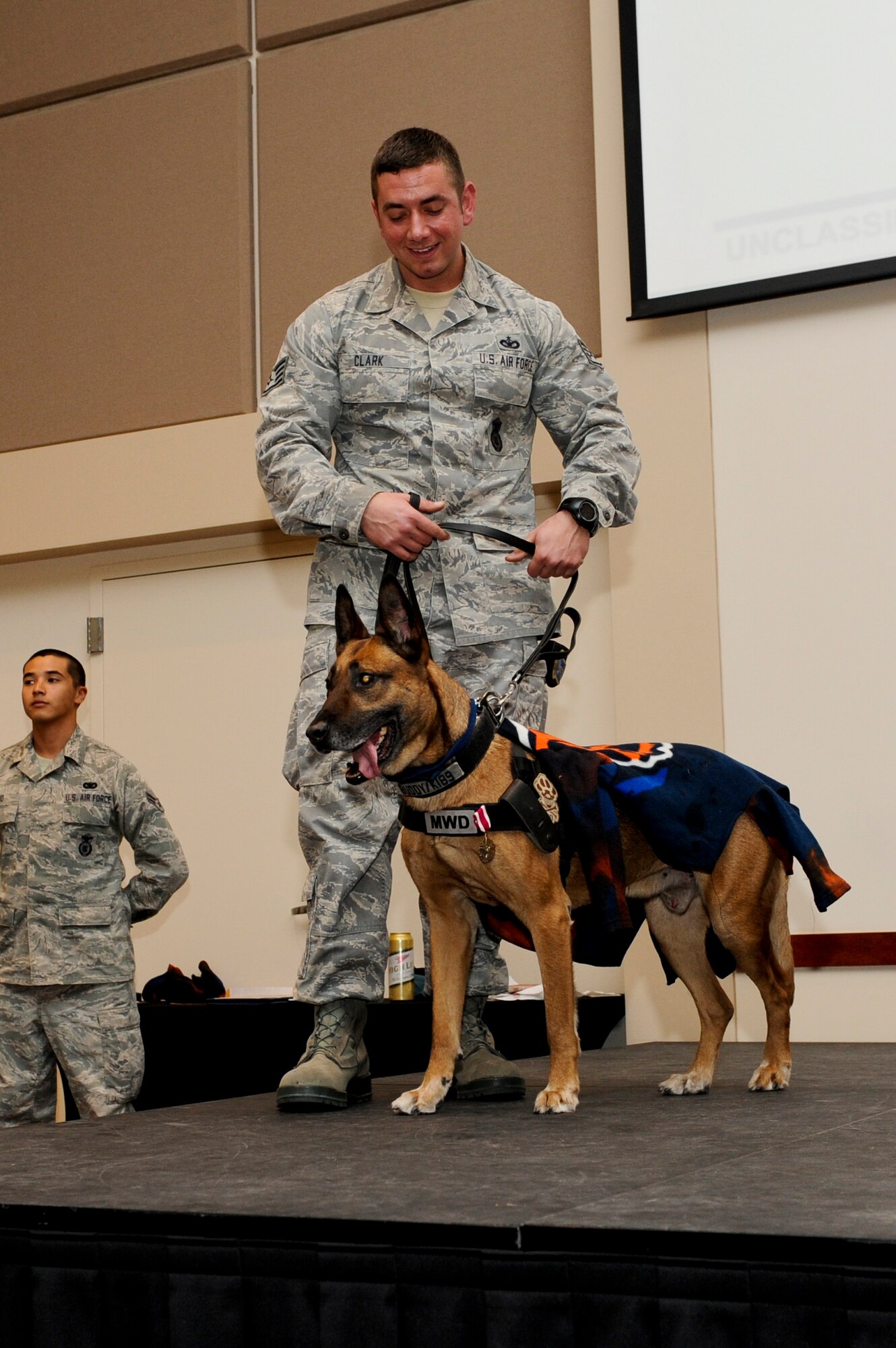 Staff Sgt. Michael Clark, 460th Security Forces Squadron military working dog handler, presents Buddy, 460th SFS military working dog retired, at the conclusion of his retirement ceremony Nov. 18, 2013, at the Leadership Development Center on Buckley Air Force Base, Colo. Buddy retired after nearly nine years of service and five deployments. After the ceremony Buddy went home to live with his handler of three years. (U.S. Air Force photo by Senior Airman Marcy Copeland/Released)