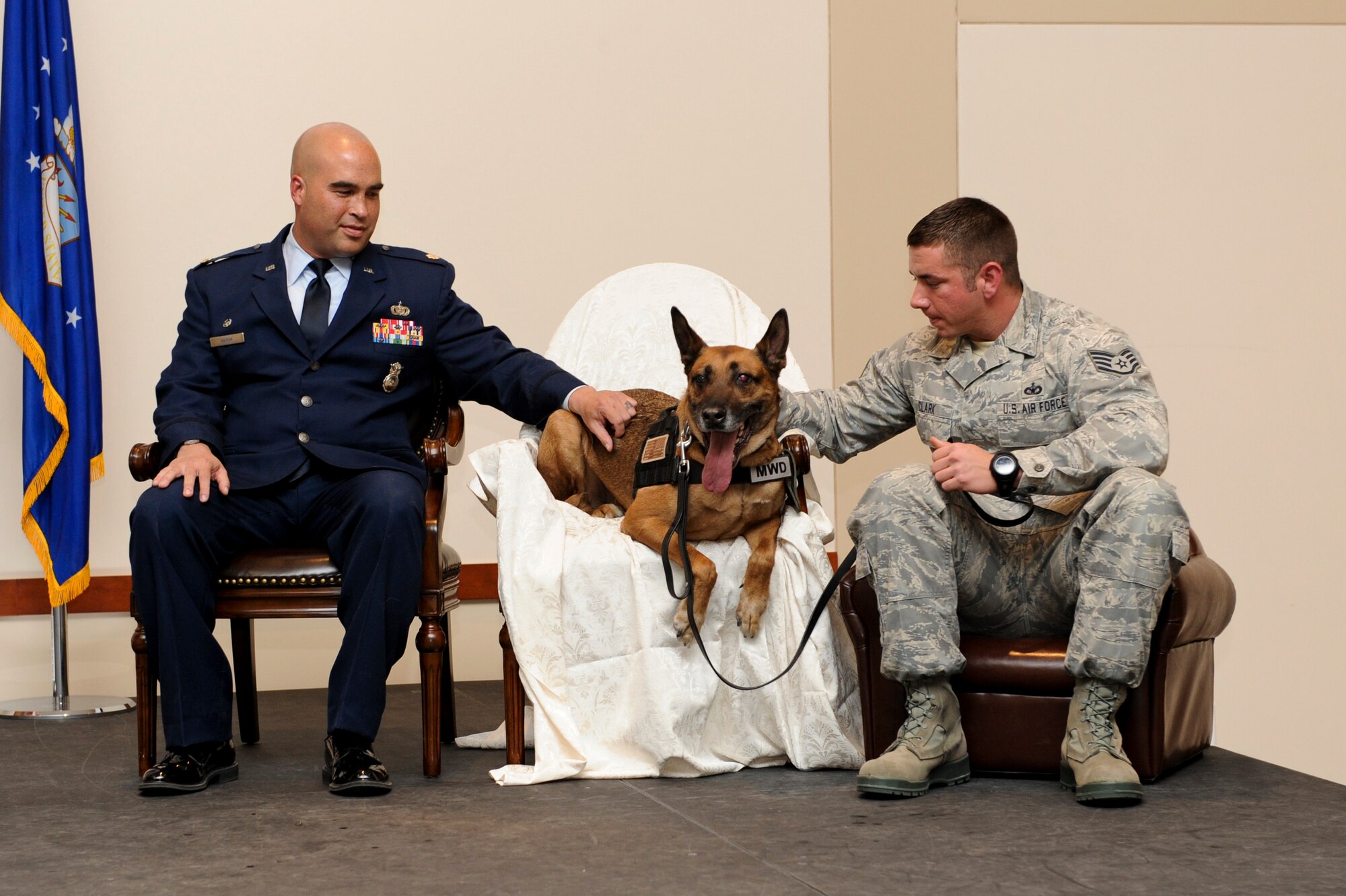 Buddy, 460th Security Forces Squadron military working dog, sits between Maj. David Haigh, 460th SFS commander, left, and Staff Sgt. Michael Clark, 460th SFS MWD handler, during Buddy’s retirement Nov. 18, 2013, at the Leadership Development Center on Buckley Air Force Base, Colo. Buddy retired after nearly nine years of service and five deployments. After the ceremony Buddy went home to live with his handler of three years. (U.S. Air Force photo by Senior Airman Marcy Copeland/Released)