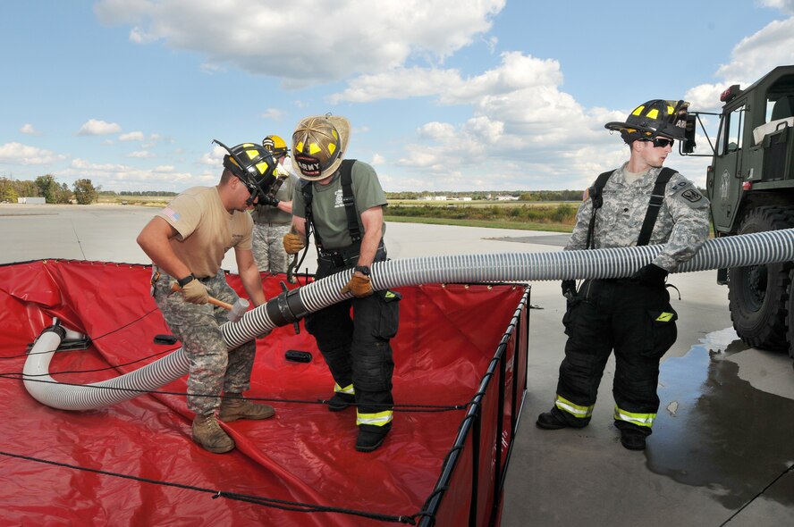 U.S. Army Specialist Gindelsperger holding the suction, Staff Sgt. Tim Layton, Non-Commissioned Officer in Charge with spanner wrench and Specialist Knight holding mallet, all from the North Carolina Army National Guard, 430th Engineer Fire-Fighting Team prepare to attach a hose to pump water into a US Army's Tactical Fire Fighting Truck during a training exercise held at the 145th Air National Guard Regional Training Site in New London, N.C., October 23, 2013.  In the wake of the Federal Government shutdown many North Carolina State firefighters were furloughed and Army Guard Firefighters assigned to 430th and 677th Engineer Fire Fighting Teams were mobilized to assist in support of Fire Protection at Charlotte-Douglas International Airport and Stanly County Airport. (Air National Guard photo by Master Sgt. Patricia F. Moran/ Released)