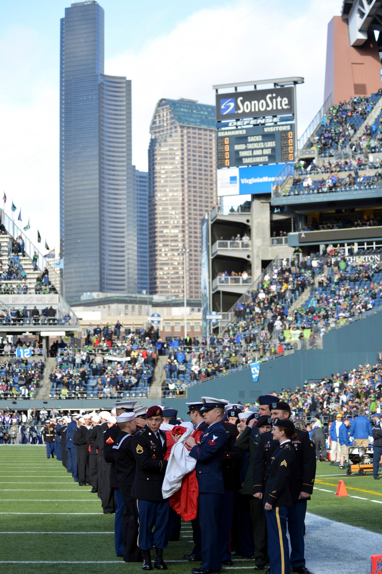 A group of Airmen, Soldiers, Sailors, Marines, and Coast Guardsmen stand on the Seattle Seahawks football field holding a field-sized American flag prior to the start of the opening ceremony, Jan. 17, 2013 in Seattle, Wash. More than 150 military members participated in the Seahawks “Salute to Service” pregame and halftime ceremonies. (U.S. Air Force photo/Staff Sgt. Jason Truskowski)