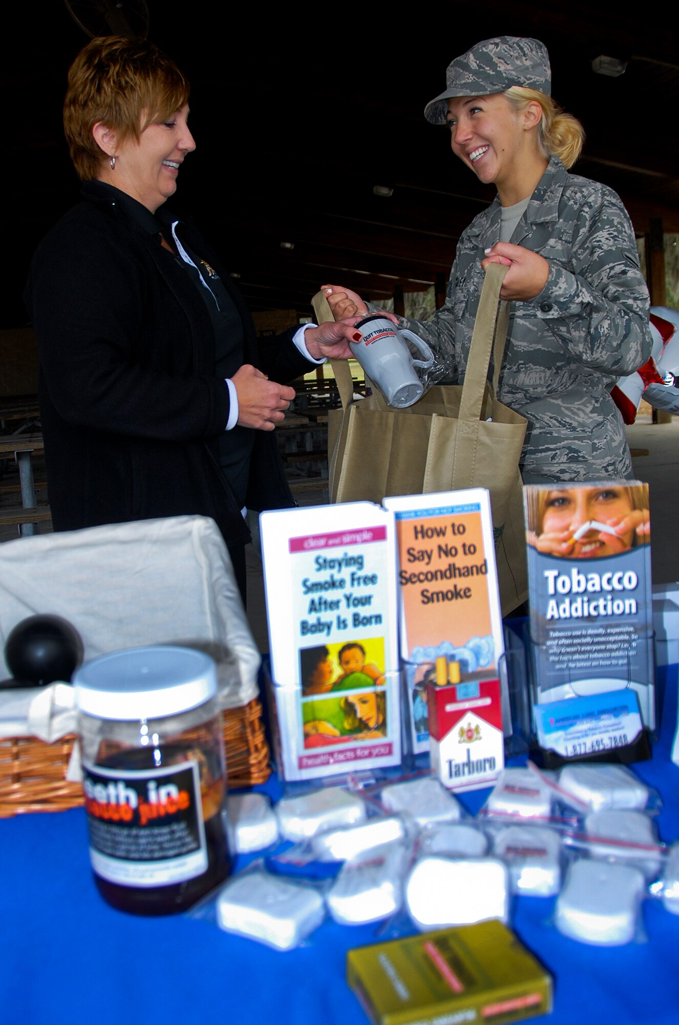 Allison DeCaro, flight chief and health promotion manager at the Health and Wellness Center, hands educational materials to Airman Blaze Bickley, of the 96th Aerospace Medicine Squadron, at the Great American Smokeout event Nov. 21 at Eglin Air Force Base, Fla.  Tobacco cessation pamphlets, coffee, mugs, gum and stress balls were given out.  Personnel from the 96th Civil Engineering Squadron issued new or recycled cigarette butt cans and signs to facility managers, for placement at designated tobacco use areas around the base.  (U.S Air Force photo/Kevin Gaddie)