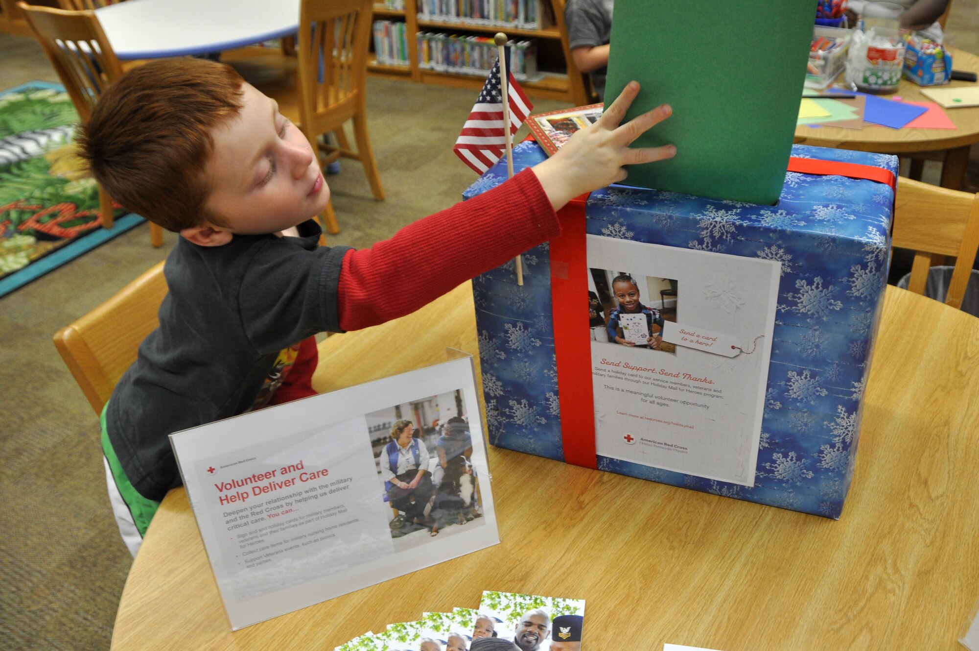 Service member son reaches over to drop off the holiday card he made for a military member during the Holiday Mail for Heroes event Nov. 19, 2013 at the Tyndall Library. Children and adults gather at the Tyndall library to make holiday cards for Veterans, service members and wounded warriors. (U.S. Air Force photo by Airman 1st Class Sergio A. Gamboa)
