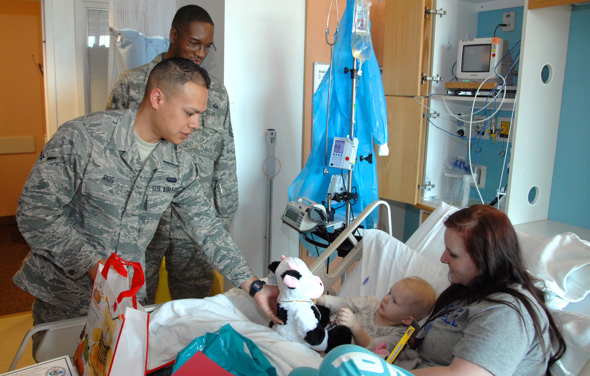 Airman Evan Rios (left), a 55th Strategic Communications Squadron communications operator, and Master Sgt. Don Mitchell, a 55th Force Support Squadron manpower analyst, both stationed at Offutt AFB, NE, deliver a stuffed cow to Madeline Dougherty, 2, who is appropriately nicknamed ‘moo-moo’, during a visit to Children’s Hospital & Medical Center in Omaha, NE, Nov. 20. They were part of a group of 12 volunteers who delivered over 90 stuffed animals on behalf of the Air Force Sergeants Association, Chapter 984. The special Noah’s Ark Workshop animals included 64 monkeys, puppy dogs, bears and cows that were assembled by Offutt members. These animals included an internal pouch where patients could place a star after making a wish. All of the animals were made available through donations to Chapter 984 of the AFSA. (U.S. Air Force photo by Delanie Stafford/Released)