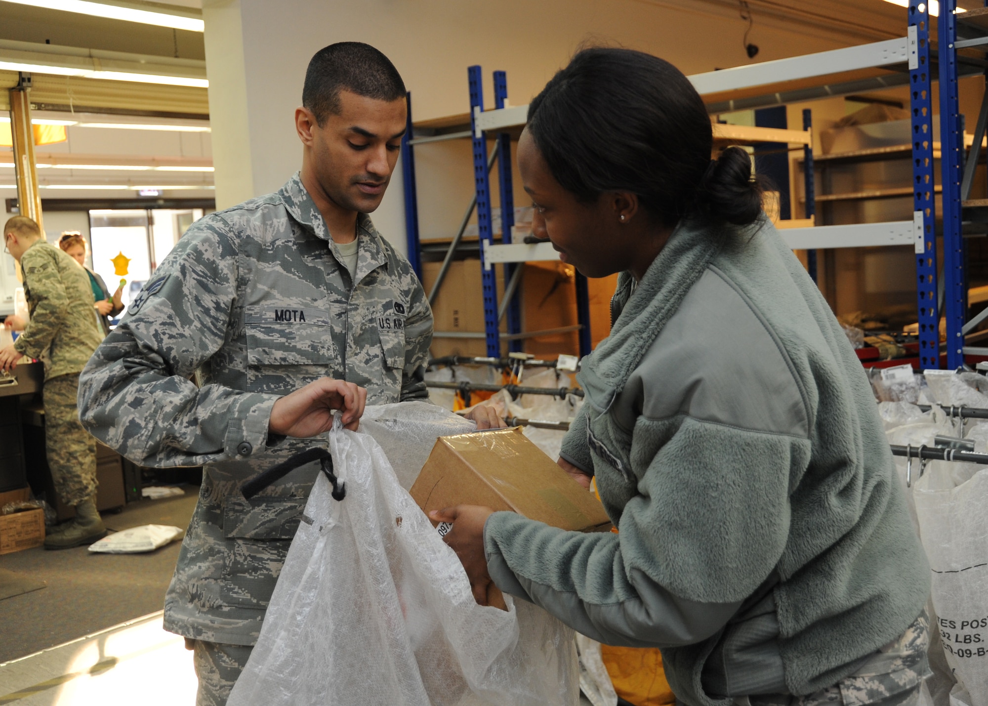 SPANGDAHLEM AIR BASE, Germany --- Senior Airmen David Mota and Jasmine Williams, both postal specialists with the 52nd Communication Squadron, place a box of mail in a bag for shipping at the post office Nov. 20, 2013. Postal specialists sort and ship hundreds of packages and letters for Spangdahlem Airmen each day. (U.S. Air Force photo by Airman 1st Class Dylan Nuckolls/Released)