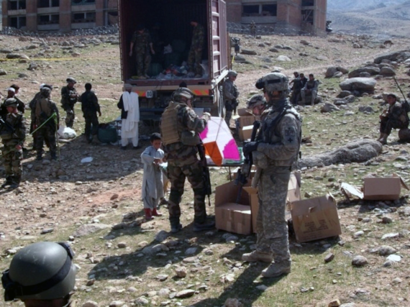 A French Soldier prepares a kite for an Afghan boy, while Sgt. Michael Mangulabnan of 3rd platoon, Company C 1st Battalion, 178th Infantry Regiment provides security and looks on during a humanitarian assistance drop on March 19.