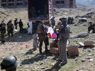 A French Soldier prepares a kite for an Afghan boy, while Sgt. Michael Mangulabnan of 3rd platoon, Company C 1st Battalion, 178th Infantry Regiment provides security and looks on during a humanitarian assistance drop on March 19.