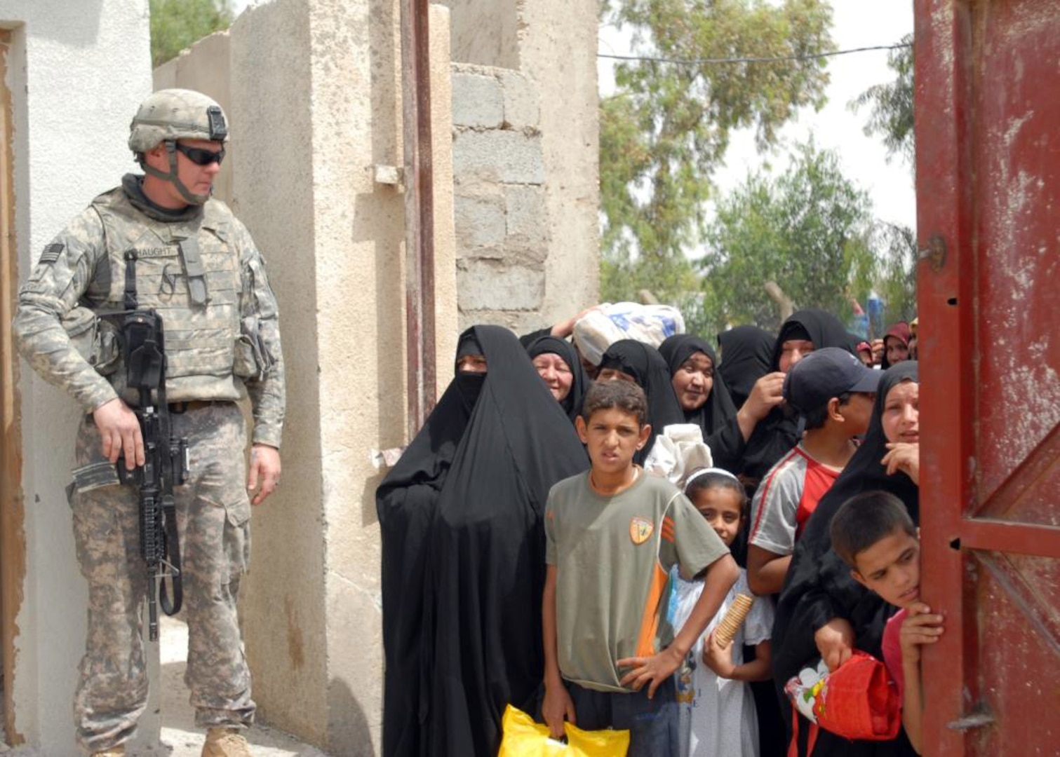A soldier stands guard as Iraqi women wait to receive food aid from the Iraqi National Police in Taji, Iraq, May 16, 2009. Multinational Division Baghdad civil affairs soldiers with the Pennsylvania National Guard's 56th Stryker Brigade Combat Team coordinated with the Iraqi National Police to release 12 pallets of United Nations relief food discovered in a warehouse to Iraqi widows.