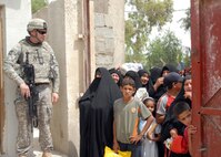 A soldier stands guard as Iraqi women wait to receive food aid from the Iraqi National Police in Taji, Iraq, May 16, 2009. Multinational Division Baghdad civil affairs soldiers with the Pennsylvania National Guard's 56th Stryker Brigade Combat Team coordinated with the Iraqi National Police to release 12 pallets of United Nations relief food discovered in a warehouse to Iraqi widows.