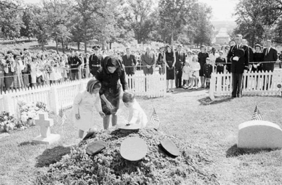 Caroline, Jacqueline, and John F. Kennedy, Jr., place flowers at the base of the eternal flame.