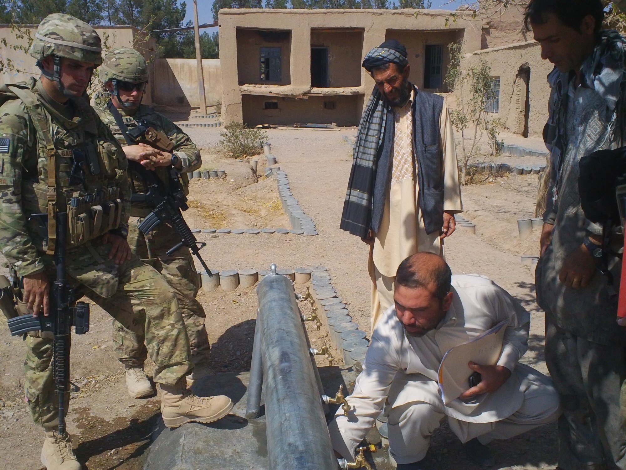 Second from left, Capt. Benjamin Knost lends his engineering expertise to provide the final inspection of a water well installed at a local school in Afghanistan as part of the civil affairs program he participated in while deployed to Shindand Air Base, Afghanistan earlier this year. Courtesy photo
