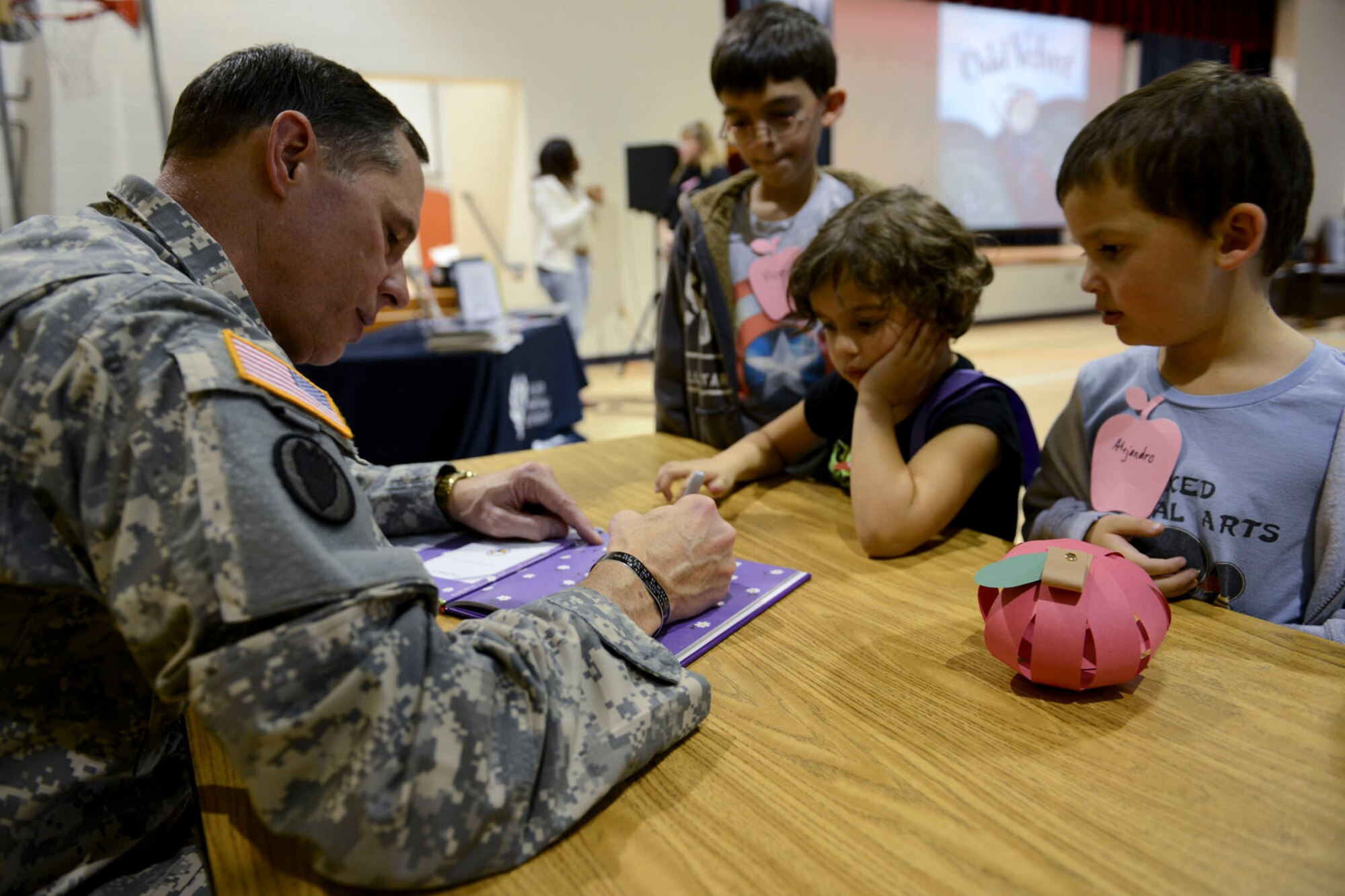 U.S. Army Lt. Gen. Keith C. Walker, Army Capabilities Integration Center deputy commanding general, signs a copy of “Odd Velvet” for Vicente, 8, Alejandro and Olivia, both 5, children of Maj. Roberto Nunez, U.S. Army Training and Doctrine Command network engineer, after the “Tell Me a Story” event at General Stanford Elementary at Fort Eustis, Va., Nov. 21, 2013. The books read to military children as part of the TMAS program highlight resiliency and optimism. (U.S. Air Force photo by Staff Sgt. Ciara Wymbs/Released)