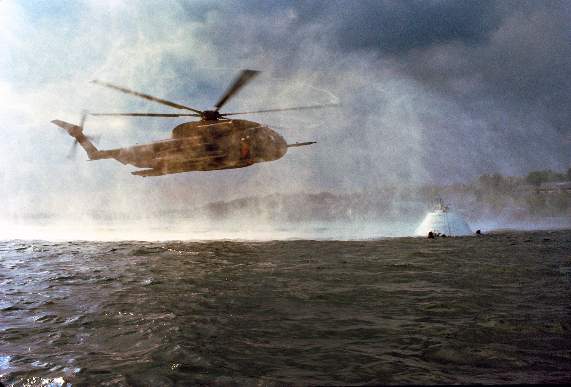 An HH-53 Super Jolly Green Giant helicopter crew and a handful of pararescuemen from the 67th Aerospace Rescue and Recovery Squadron, RAF Woodbridge, train for recovery operations with a mockup of the Apollo space capsule Mar. 4, 1982. The capsule now sits outside the 920th Rescue Wing's pararescue squadron at Patrick AFB, Fla. The 920th is responsible for range-clearing and safety on all launches from Cape Canaveral Air Force Station, and was in charge of astronaut recovery and contingency response for all NASA space shuttle flights. (U.S. Air Force photo/Staff Sgt. Ken Hammond)