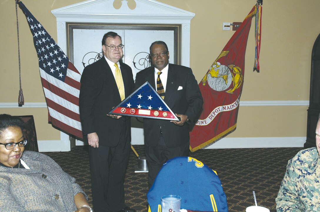Johnny L. Litman III, right, procurement and fiscal law attorney, Office of Counsel, Marine Corps Logistics Command, receives an American flag and shadow box from David Rowland, attorney, Office of Counsel, LOGCOM, during Litman’s retirement luncheon Nov. 14 held at the Town and Country Restaurant Ballroom.