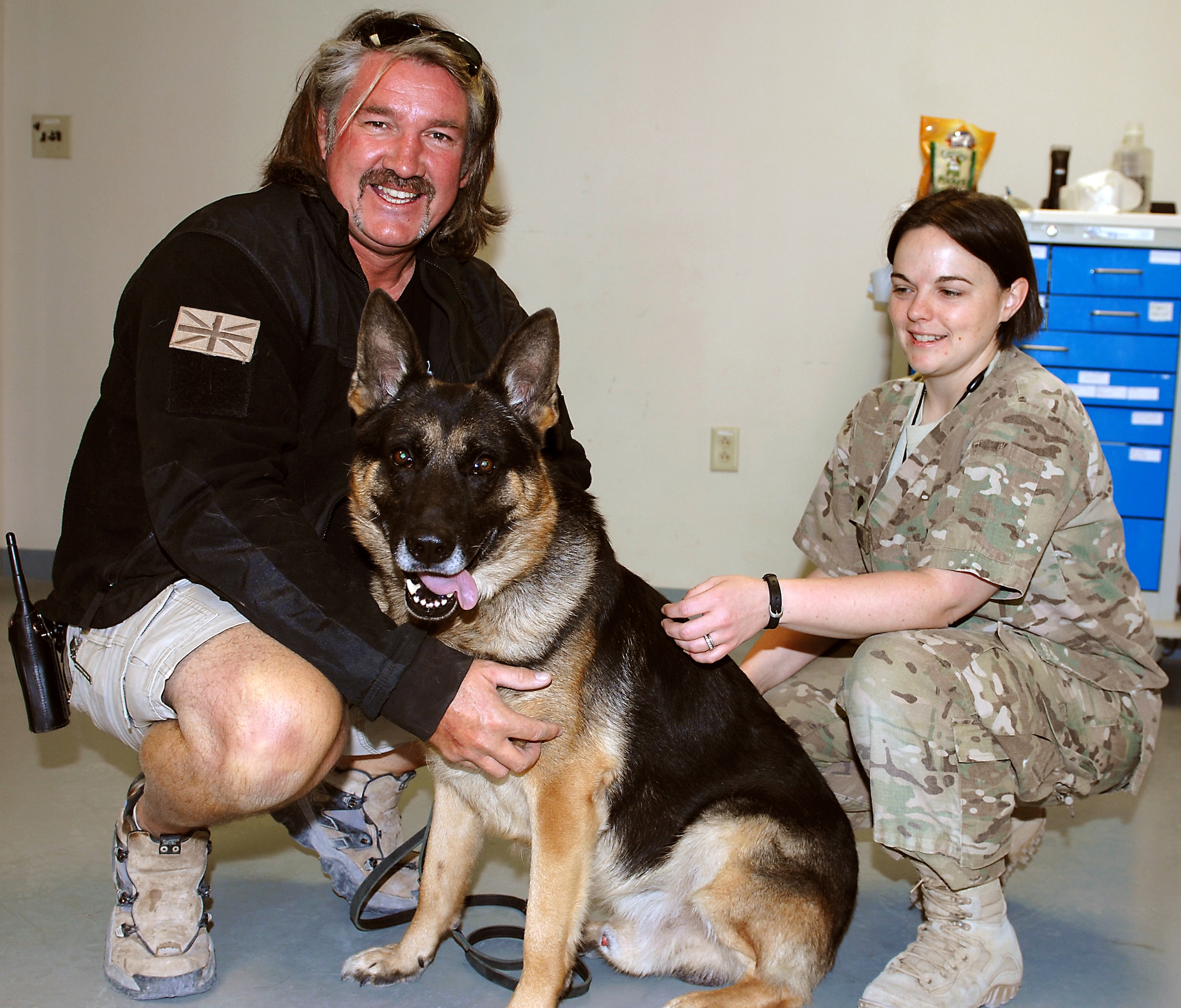 Contract Working Dog Tommi and his handler, Simon Williams (left), Vigilant Canine Services International pose for a photo with U.S. Army Spc. Nicole Lamanna (right), Kandahar Veterinary Treatment Facility animal care specialist, before a routine procedure Nov. 20, 2013, at Kandahar Airfield, Afghanistan. Tommi’s visit was for a routine dental cleaning. (U.S. Air Force photo by Senior Airman Jack Sanders)