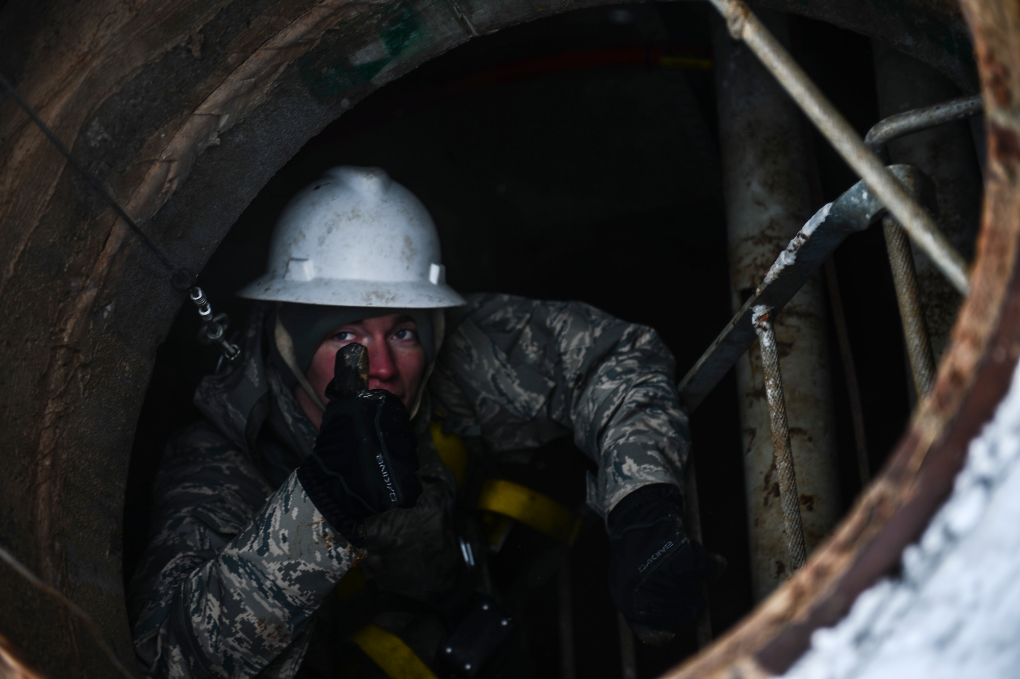 Airman 1st Class Aaron Thompson, 460th Space Communications Squadron cable antenna systems technician, signals to be hoisted up during confined-spaces training Nov. 21, 2013, near the 460th SCS building on Buckley Air Force Base, Colo. Regardless of the weather, cable antenna systems technicians are required to complete confined-spaces training as part of on-the-job training. (U.S. Air Force photo by Senior Airman Riley Johnson/Released)