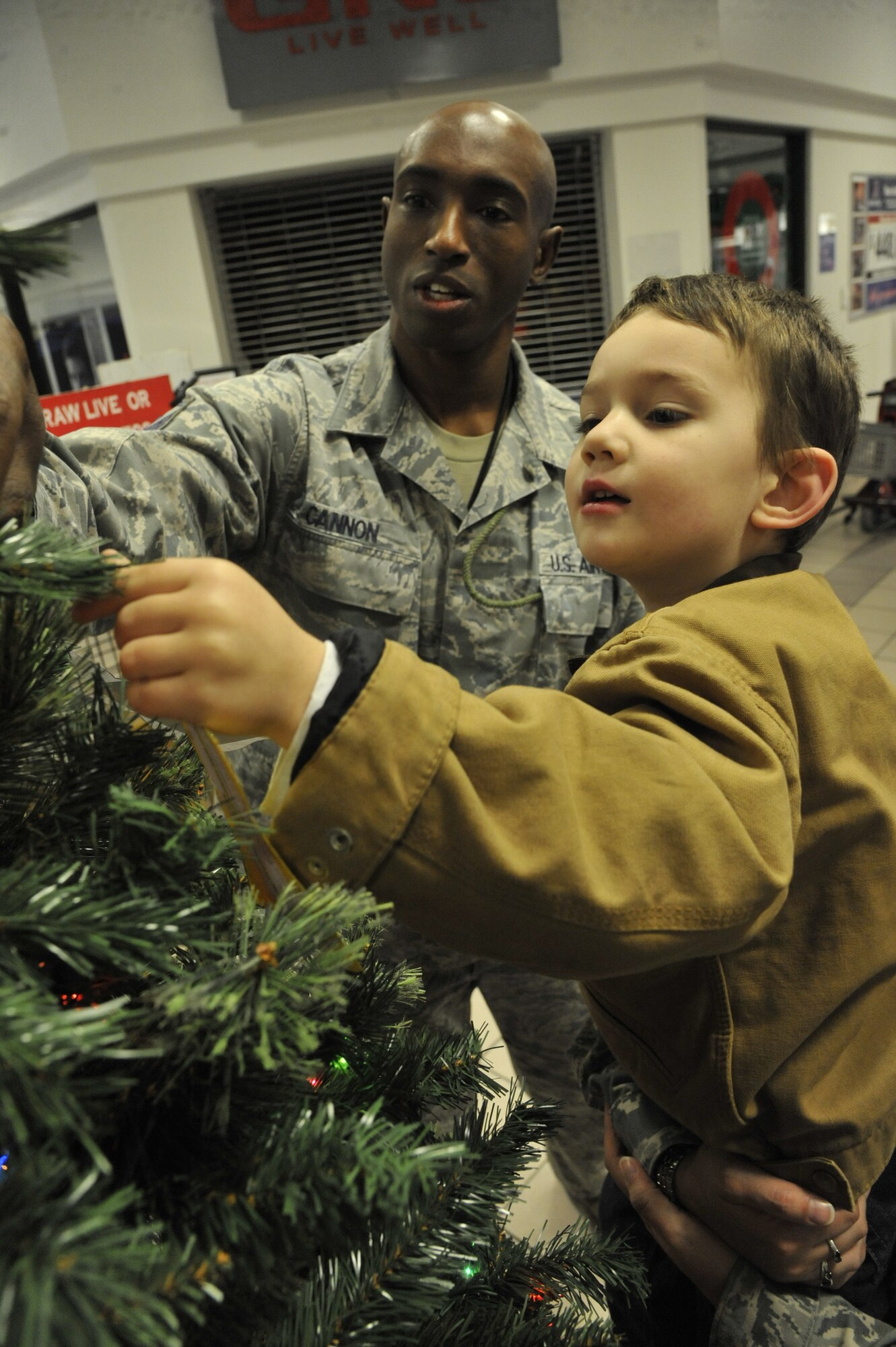 Master Sgt. Oscar Cannon, 509th Aircraft Maintenance Squadron first sergeant, and Alexander Vitela, 3, son of Tech. Sgt. Kassandra Vitela, 325th Weapons Squadron, place an angel on the angel tree at Whiteman Air Force Base, Mo., Nov. 19, 2013. Donors who participate in this program choose an angel, buy an age appropriate gift, and place the gift and angel under the tree. (U.S. Air Force photo by Airman 1st Class Keenan Berry/Released)
