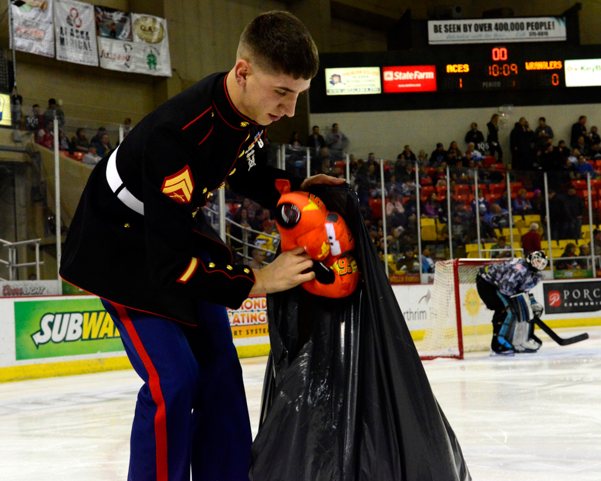 Marine Cpl. James Johnston, Detachment Military Police Company D, 4th Law Enforcement Battalion, collects toys for Toys for Tots during intermission of an Alaska Aces hockey game at Sullivan Arena in Anchorage Nov. 16. The Aces organization hosted Military Appreciation Nights during games Nov. 15 and 16. Activities included a ceremonial puck drop by Air Force Lt. Gen. Russell Handy, Alaska Command and 11th Air Force commander, a tug-of-war between members of various branches of service and a presentation of Aces jerseys to leaders of each branch of service represented at JBER. (U.S. Air Force photo/Airman 1st Class Carly Kavish)